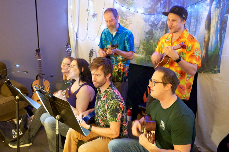 Six people playing ukuleles and singing.