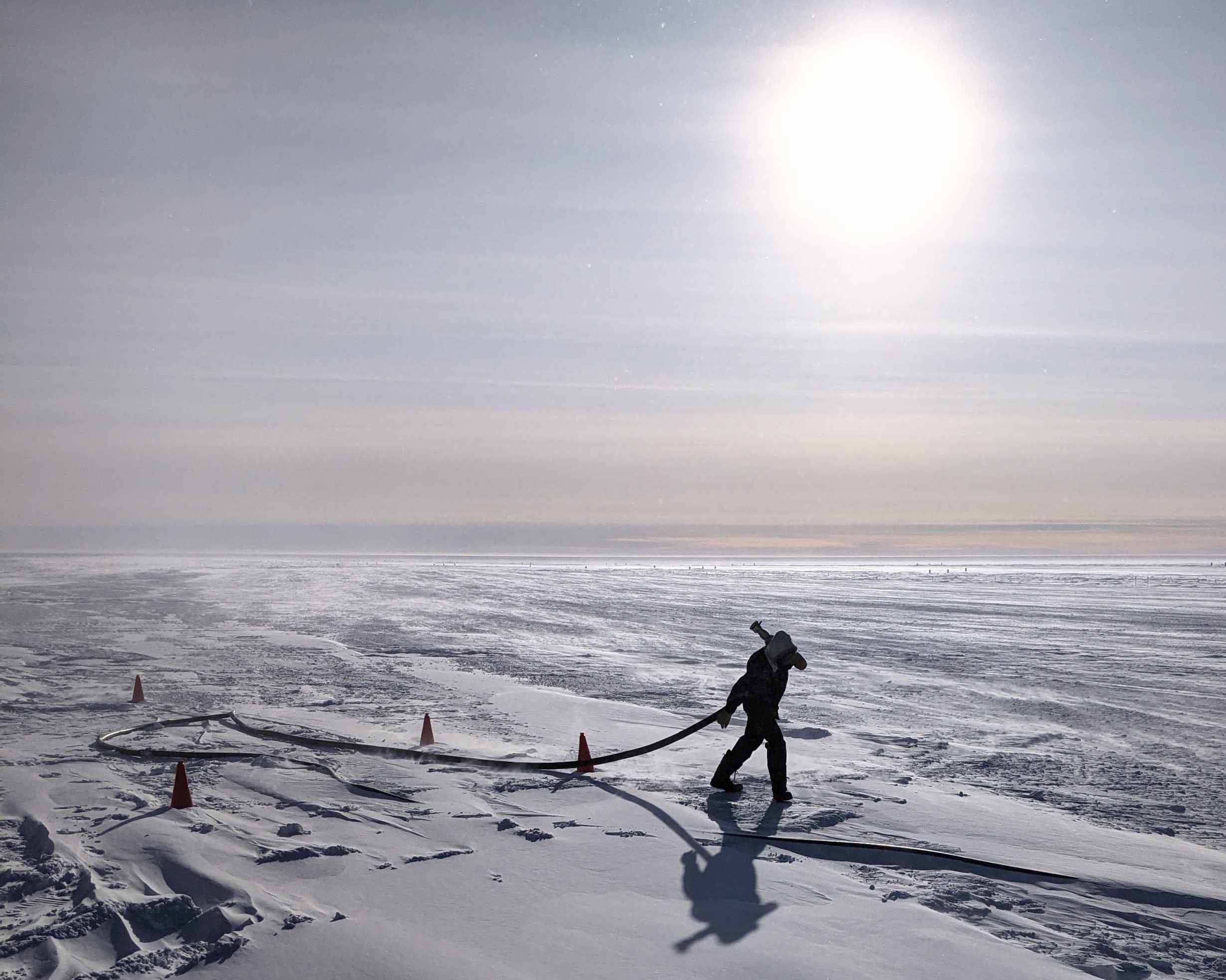 Person hauling large fuel hose out on the South Pole ice.