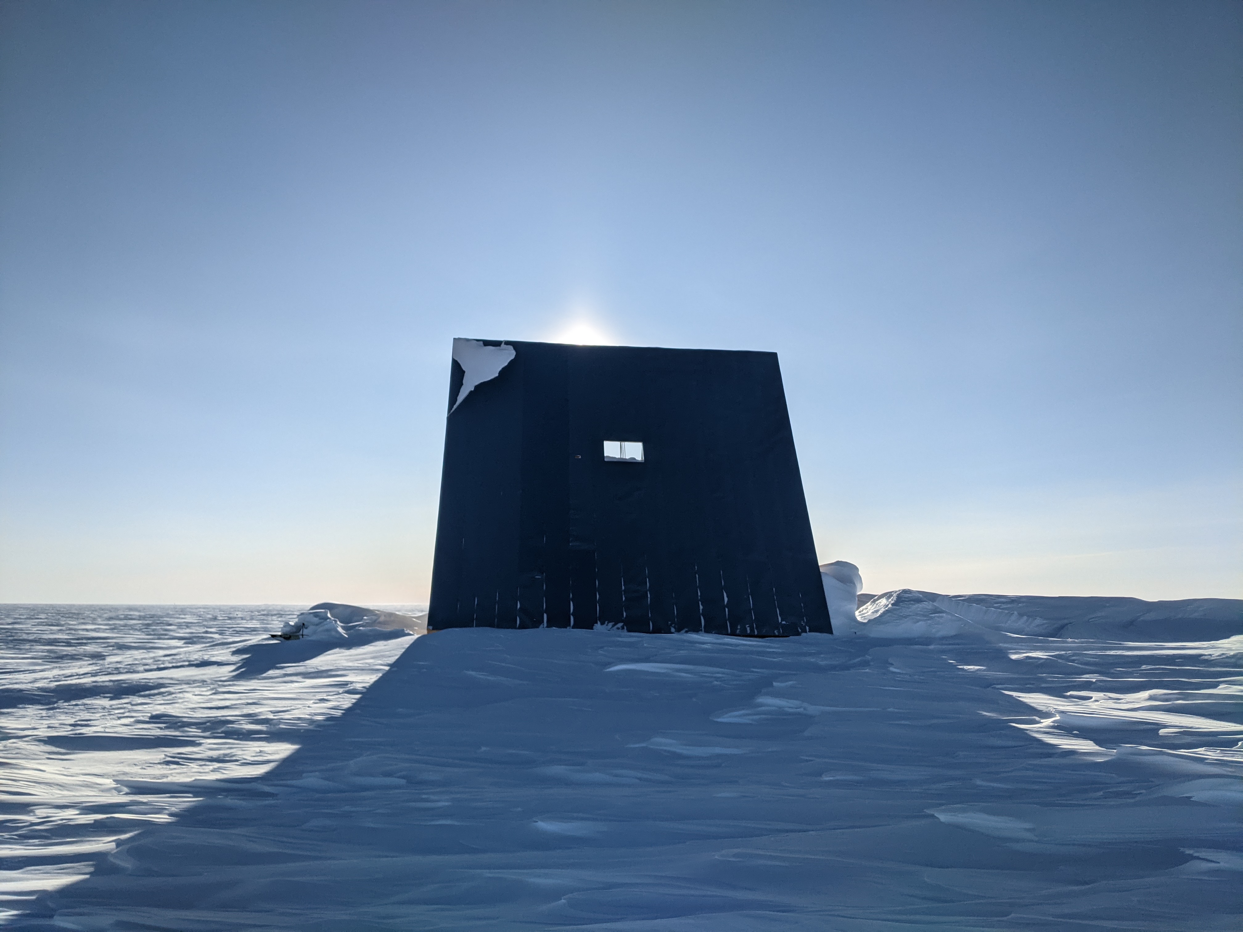 Large monolithic structure outside at the South Pole, with sun shining from behind it.