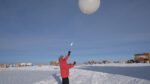Winterover in red parka out on the ice, just after launching a weather balloon.