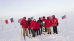 Group of winterovers posing around the post at the ceremonial South Pole.