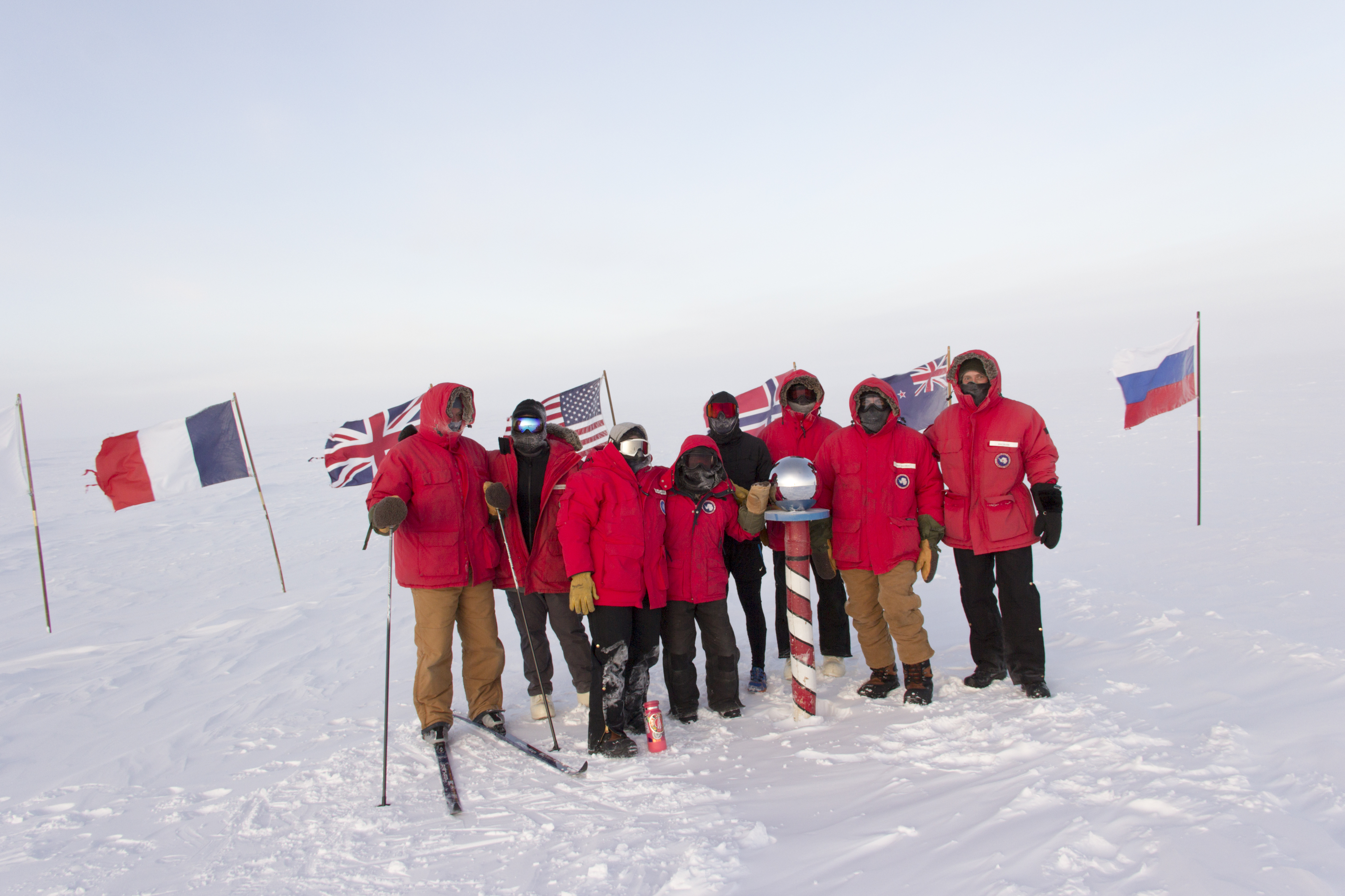 Group of winterovers posing around the post at the ceremonial South Pole.