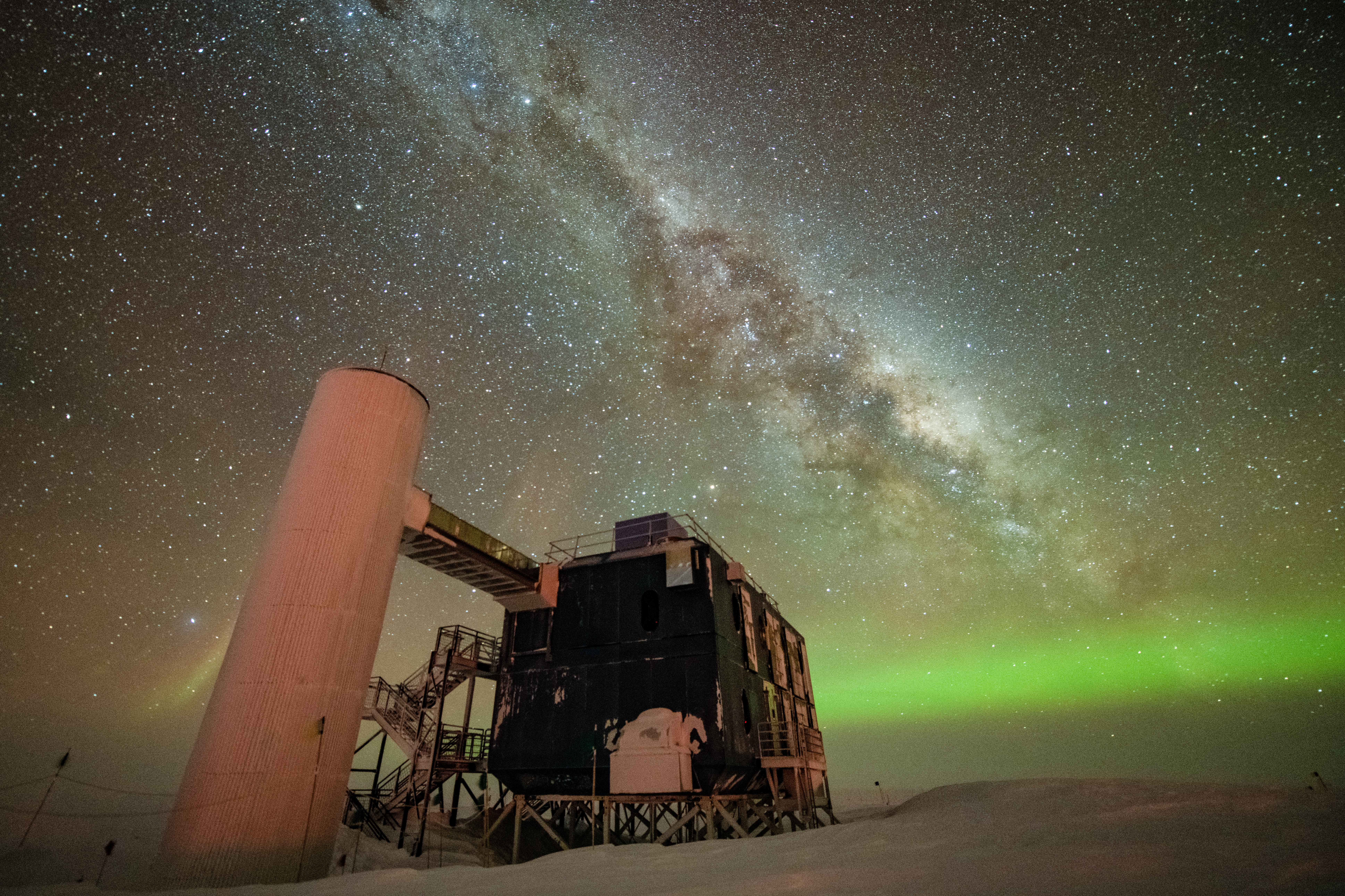 The IceCube Lab is seen with a starry, night sky and Milky Way in the backdrop over the northern lights