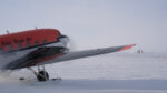 Small plane in foreground parked on the ski way, IceCube Lab off in distance on horizon.