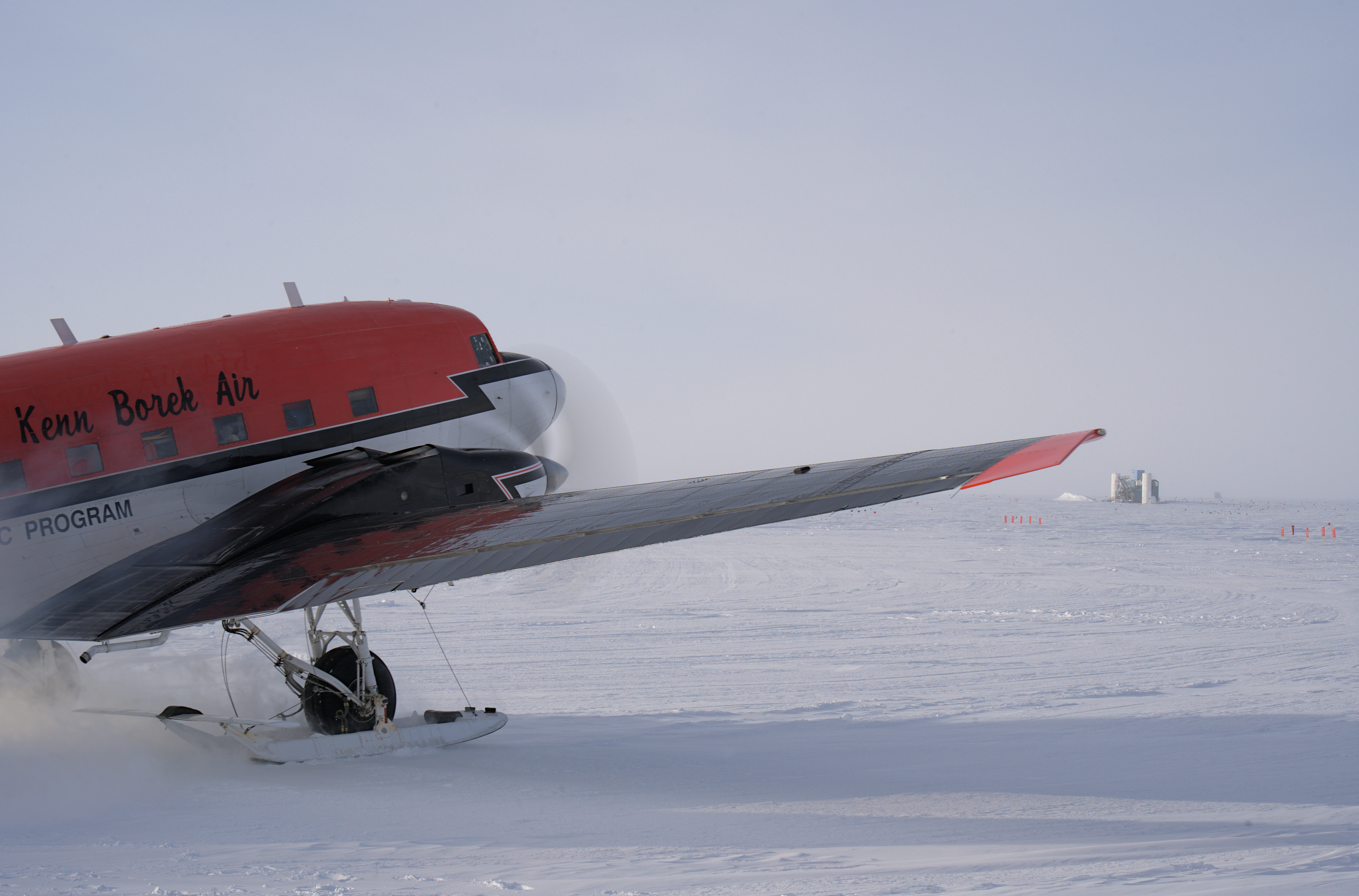 Small plane in foreground parked on the ski way, IceCube Lab off in distance on horizon.