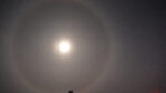 A bright moon with large moon halo at the South Pole, with South Pole Telescope seen in shadow in the distance.